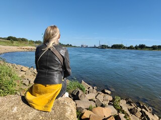 Blonde Frau sitzt am Flussufer vom Rhein