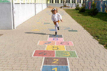 Junior schoolgirl playing hopscotch in school yard