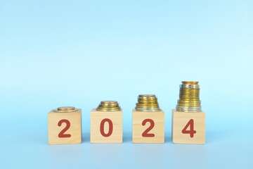 Year 2024 financial success, save, invest and grow money concept. Increasing stack of coins in wooden blocks.