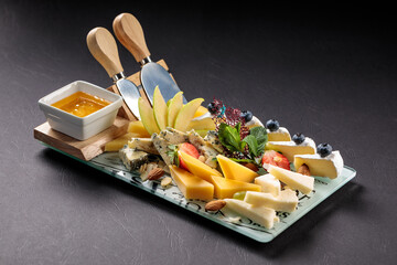 
Snack board with different types of cheese, fruits, berries and knives on a black background