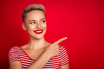 Portrait of young beautiful lady pointing finger novelty look curious sharing useful information with you isolated on red color background