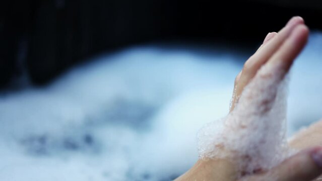 female hand in foam in black wooden bath. close-up the girl takes a bath