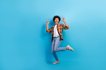 Fototapeta na wymiar Full length photo of carefree cool guy wear plaid shirt dancing showing hard rock signs empty space isolated blue color background
