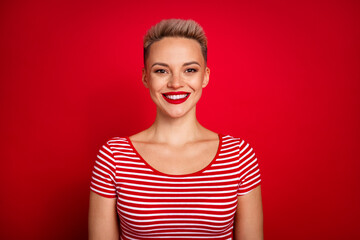 Portrait of attractive young pretty woman short haircut wearing striped stylish t shirt toothy smiling isolated on red color background