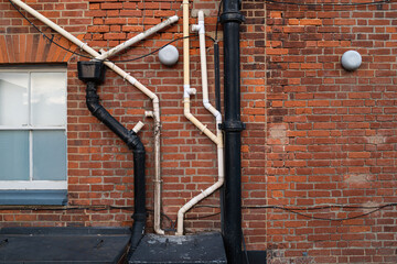 Old brick built apartment building showing a mass of plumping and drainage pipes. Seen next to a...