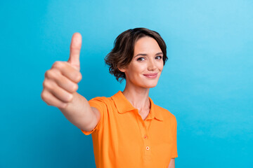 Photo of cheerful confident girl dressed orange polo showing you thumb up isolated blue color background