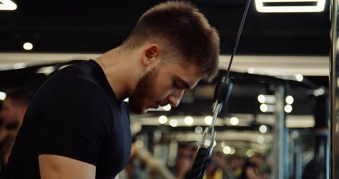 Medium shot of athletic handsome young man performing bench press in gym. Man wears black long sleeve compression shirt, blue shorts. Facial muscles work. High quality 4k footage