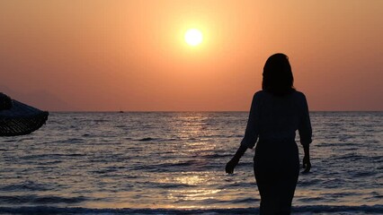 silhouette of woman walking alone on the beach at sunset - Powered by Adobe