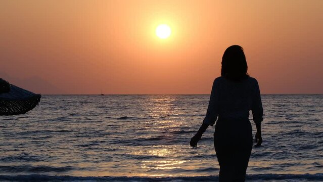silhouette of woman walking alone on the beach at sunset