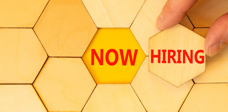 Now hiring symbol. Concept words Now hiring on beautiful wooden puzzle. Beautiful yellow background. Businessman hand. Business marketing, motivational now hiring concept. Copy space.