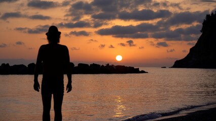 silhouette  of single man alone admire the fiery sunset with red sky by the sea - desire for holidays and Caribbean colors in the sky - experience the beauty of nature