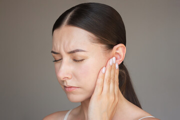 a young woman is in pain, closing her eyes, pressing her palm to her ear, suffering from otitis. Deafness, ear inflammation.