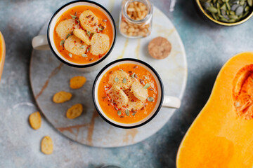 Roasted butternut squash soup with cream and pumpkin seeds on two white mugs.