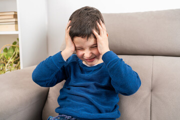 Child suffering headache sitting on a sofa in the living room at home