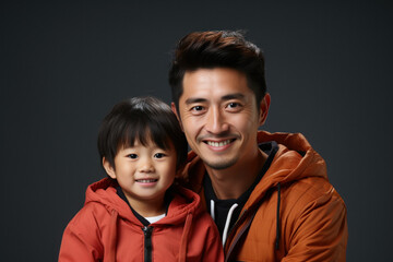 Dad holding in arms little son in casual clothes on dark gray background