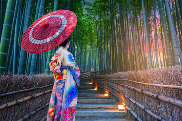 Beautiful Asian girl in kimono holding an umbrella visits a bamboo forest in Kyoto, Japan.