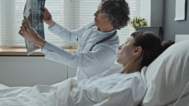 Medium shot of middle-aged female physician checking up her patient and showing results of scanning