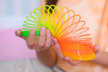 Child playing orange and green tight, colorful flexible children's toy, fun plastic toy. Teen girl plays slinky - obrazy, fototapety, plakaty