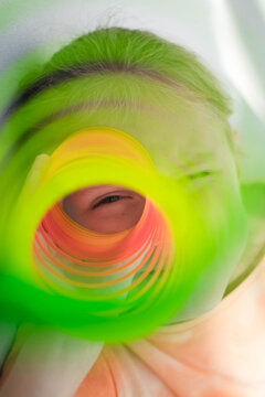 The child's eye looks through the orange-green dense, colorful flexible children's toy, fun plastic toy. Teen girl plays slinky