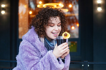 beautiful woman in trendy violet coat drinks mulled wine outdoors 