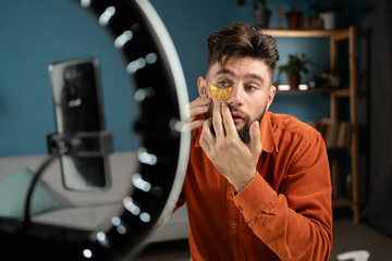 Male blogger cosmetologist recording a tutorial on the use of cosmetics leading a vlog on social networks, using patches under the eyes for skin care. Influencer selling cosmetics