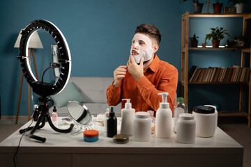 Male blogger recording tutorial video for his beauty blog about skincare routine. Vlogger applying face mask, recording video for social network. Blogging