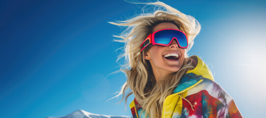 happy smiling blonde skier woman with ski goggles and colorful clothing against blue sky background on sunny day. winter vacations. banner with copy space - obrazy, fototapety, plakaty