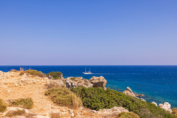 Fototapeta na wymiar View from mountain of blue water of Mediterranean sea to passing sailing yacht. Rhodes. Greece.
