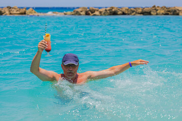 Beautiful view of happy man with cocktail glass in his hand in splashing Caribbean sea. Curacao.