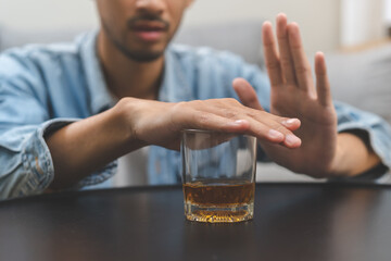 Alcoholism, depressed asian young man refuse, push out alcoholic beverage glass, drink whiskey, sitting alone at night. Treatment of alcohol addiction, having suffer abuse problem alcoholism concept.