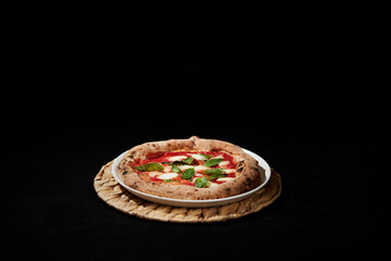 Pizza margarita sobre un plato blanco con masa madre, hojas de albahaca fresca, salsa de tomate y queso derretido