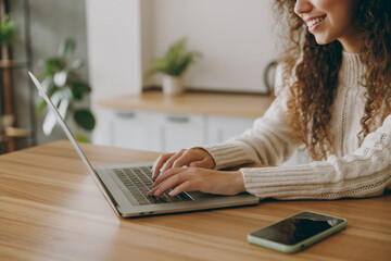 Cropped happy young fun housewife IT woman wear casual clothes sweater hold use work on laptop pc computer look for recipe sit at table in light kitchen at home alone. Lifestyle cooking food concept.