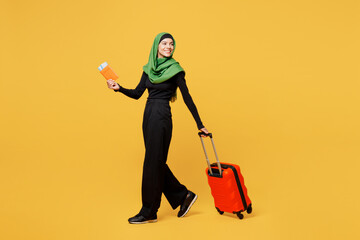 Traveler arabian asian muslim woman wear green clothes hold passport ticket bag look aside isolated on plain yellow background Tourist travel abroad in free time rest getaway. Air flight trip concept