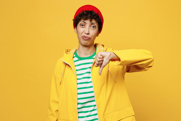 Young sad dissatisfied woman wears waterproof raincoat outerwear show thumb down dislike gesture isolated on plain yellow background studio portrait. Outdoor lifestyle wet fall weather season concept
