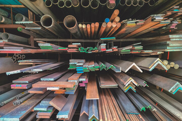 Group of various types of steel bars and metal pipes stacked on the storage shelf of building...
