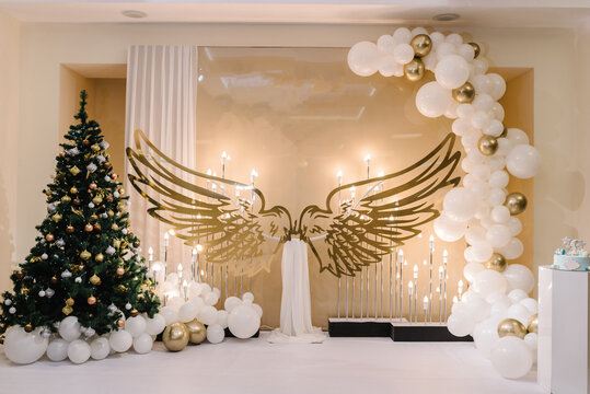 Arch with balloons, candles and angel wings in restaurant. Area for celebrating wedding, birthday or baptism with winter decor. Christmas tree decorated with garlands and ball toys. Happy New Year.