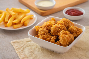 Crispy popcorn chicken in bowl with french fries on plate and sauce.