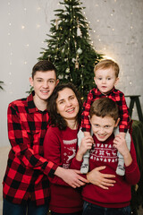 Mom hugs kids. Mother embrace children. Brothers boys portrait near Christmas tree with garland. Large big family with three children. Family holiday. Merry Christmas. Decorated interior home. Closeup