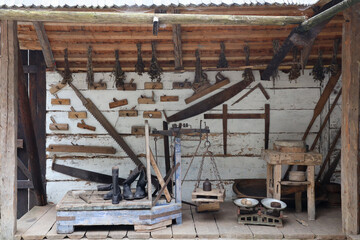Collection of planers and retro wood saws hang on a wooden wall near an old house. Carpenters plane and other things on wall - obrazy, fototapety, plakaty