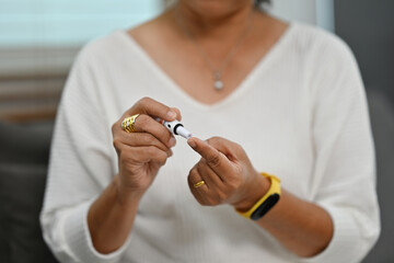 Close up with an old Asian woman using a lancet prick on her finger to check blood sugar level with a glucometer, Healthcare and Medical of diabetes concept