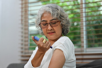 Portrait of a Diabetic mature woman taking an insulin shot on her arm. Diabetes and elderly health care concept - obrazy, fototapety, plakaty