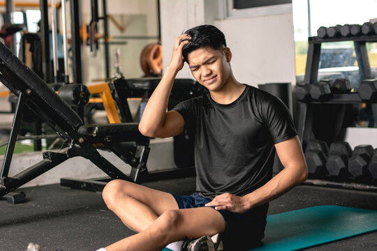 A young handsome asian man scratching his hair. Looking frustrated and disappointed at himself while sitting on the mat at the gym.