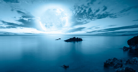 Night sky with blue moon in the clouds over the calm blue sea, many sytars in the background  "Elements of this image furnished by NASA