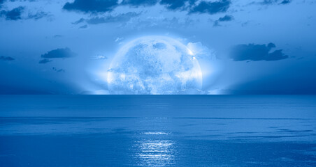 Fototapeta na wymiar Night sky with blue moon in the clouds over the calm blue sea, many sytars in the background 