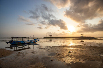 Fototapeta na wymiar Sunrise at the sandy beach of Sanur. Temple in the water. Traditional fishing boat, Jukung on the beach. Hindu faith in Sanur on Bali. Dream island and dream destination
