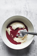 Red velvet cake batter being mixed in a white bowl, folding cake batter in a white mixing bowl, the...