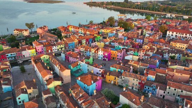 Aerial view of Burano colorful houses, along the Fondamenta embankment, featuring fishing boats and bridges, in the Venice province of the Veneto region, Italy at sunrise golden hour