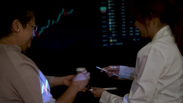 Asian woman investor advice to Asian Senior, Elderly, Retired woman  to planning investment in Stock Exchange Market. Sign on the digital tablet and shake hands.