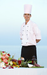 Happy man, portrait and chef on beach for cooking, resort meal or outdoor catering service. Male person or professional cook smile in fine dining, restaurant or luxury meal, food or water at sea