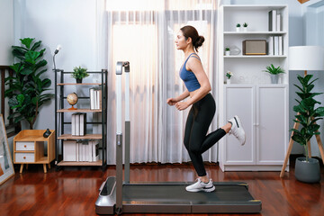 Full length side view of energetic and strong athletic asian woman running running machine at home....